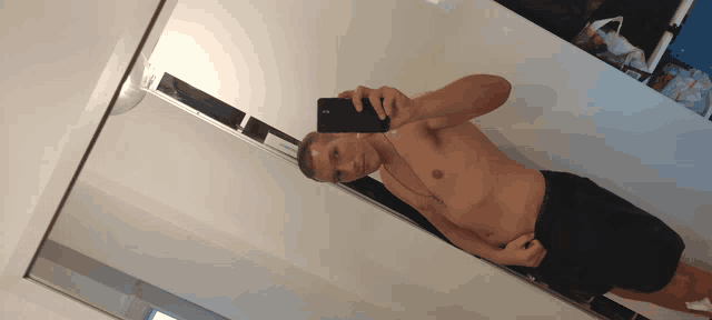 a shirtless man takes a selfie in a mirror