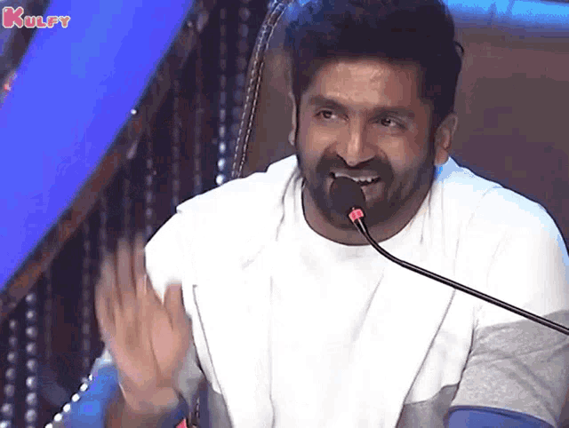 a man with a beard speaking into a microphone with the words kulfy written on the bottom