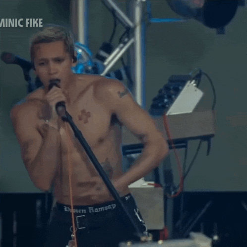 a shirtless man singing into a microphone with the words minic fike on the bottom left