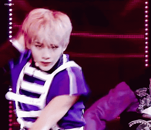 a young man is dancing on a stage in a purple and white outfit .