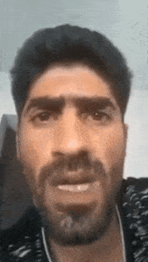 a man with a beard is making a funny face while talking to the camera .