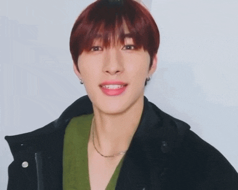 a young man with red hair is wearing a green sweater and a black jacket and looking at the camera .