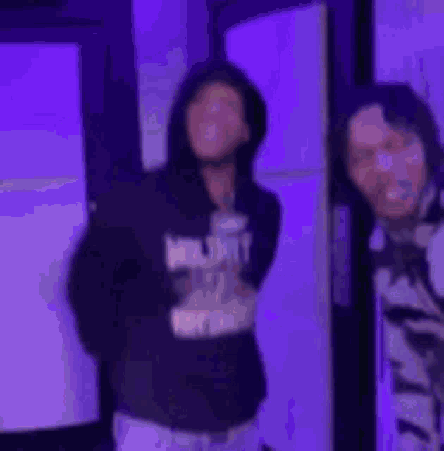 a couple of men are standing next to each other in a room with purple lights .