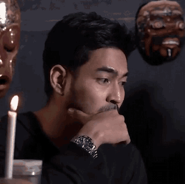 a man with a watch on his wrist is sitting in front of a candle