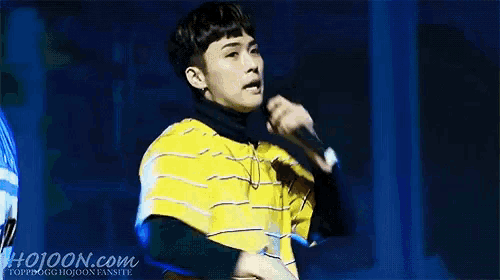 a young man in a yellow striped shirt is singing into a microphone on stage .