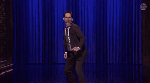 a man in a suit and tie is dancing on a stage with a blue curtain behind him .