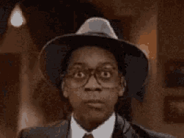 a young man wearing a hat and glasses looks at the camera .