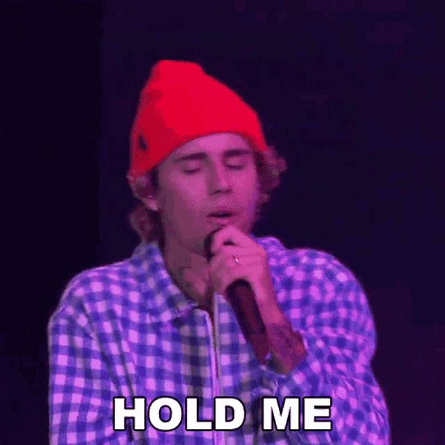 justin bieber is singing into a microphone while wearing a red hat .