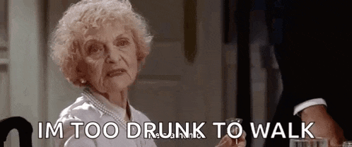 an elderly woman is sitting at a table drinking a glass of wine and says `` im too drunk to walk '' .