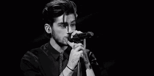 a black and white photo of a man singing into a microphone on stage .