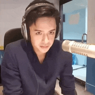 a young man wearing headphones is sitting in front of a microphone in a room .