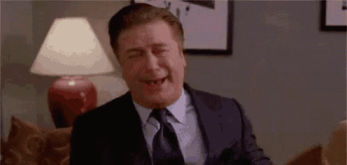 a man in a suit and tie is sitting on a couch laughing .