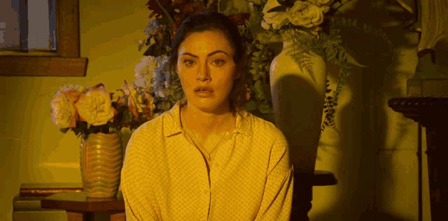 a woman in a yellow shirt is standing in front of a vase of flowers