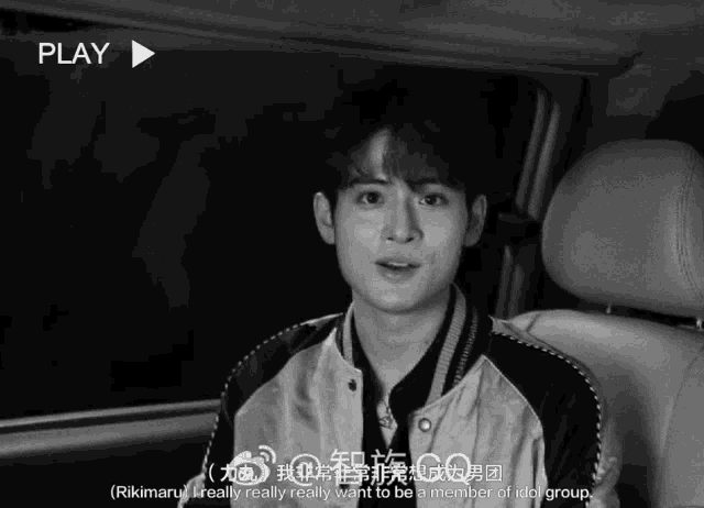 a black and white photo of a young man sitting in a car with the play button visible