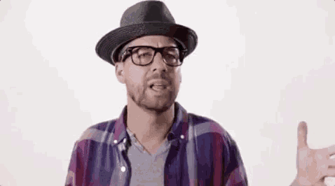 a man wearing a hat , glasses , and a plaid shirt is giving a thumbs up .