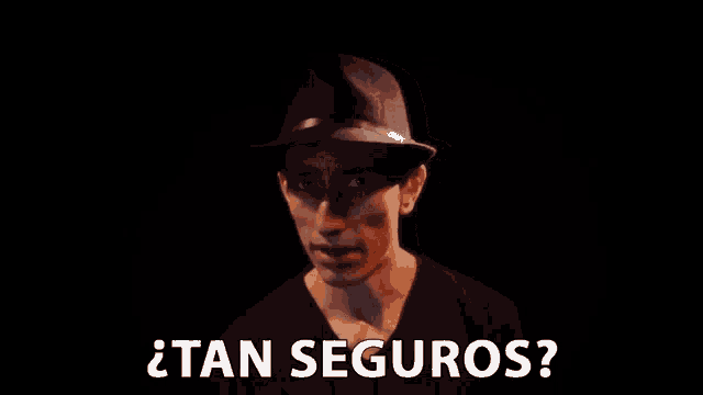 a man wearing a hat says " tan seguros " in a dark room