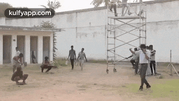 a group of people are standing around a scaffolding on a dirt field .