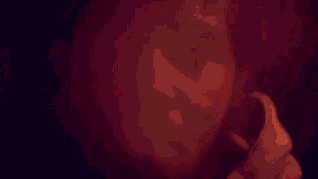 a close up of a man 's face in a dark room with a red light behind him .