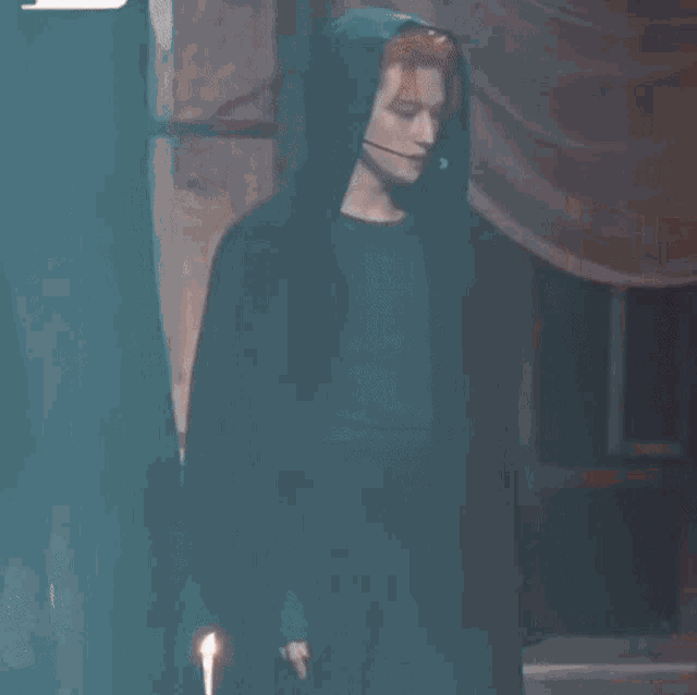 a man with red hair is wearing a black coat with a hood and microphone .