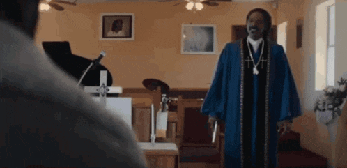 a man in a blue robe is standing in front of a microphone in a church .