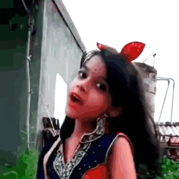 a little girl with a red bow on her head is standing in front of a building and making a funny face .