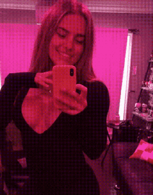a woman is taking a selfie in front of a pink curtain