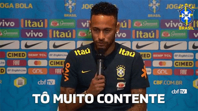 a soccer player is holding a microphone in front of a banner that says to muito contente