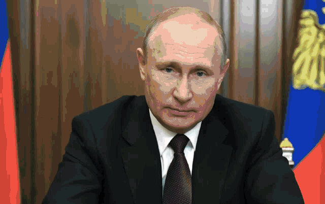 a man in a suit and tie is sitting in front of a russian flag