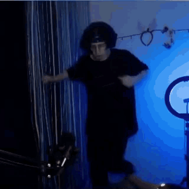 a man in a black shirt is dancing in a dark room with blue lights .