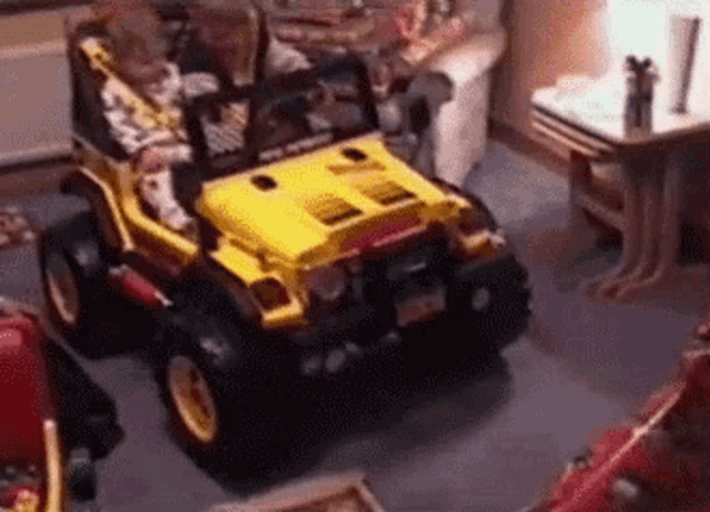 a child is driving a yellow toy jeep in a room .