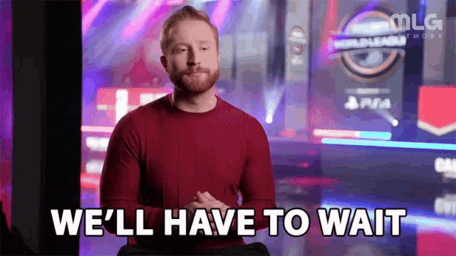 a man in a red sweater is sitting in front of a video game screen and says `` we 'll have to wait '' .