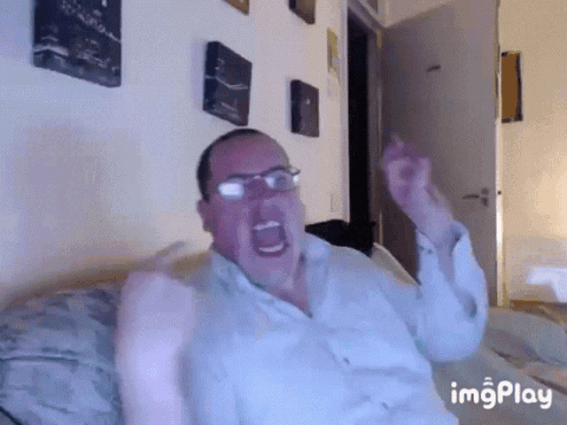 a man with glasses is sitting on a bed with his arms outstretched .