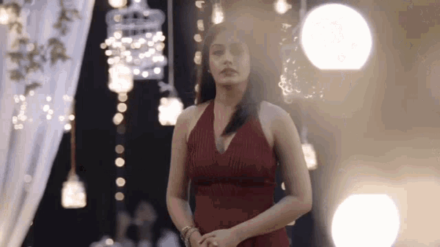 a woman in a red dress is standing in a room with a lot of lights hanging from the ceiling .