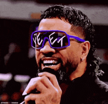 a man with a beard is wearing sunglasses and holding a microphone in his mouth .