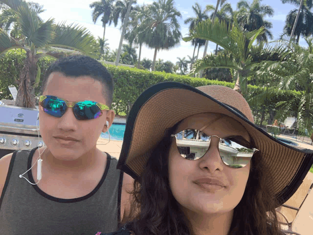 a boy wearing sunglasses stands next to a woman wearing a hat and sunglasses