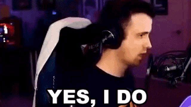 a man wearing headphones is sitting in a chair in front of a microphone and saying yes , i do