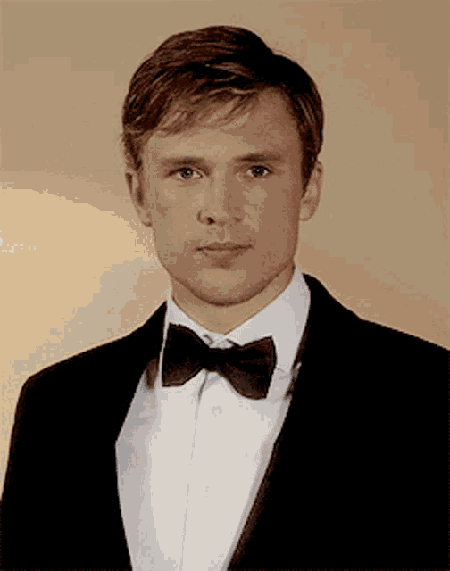 a man in a tuxedo and bow tie is looking at the camera
