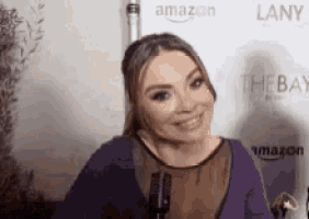 a woman is smiling in front of a microphone in front of an amazon banner .