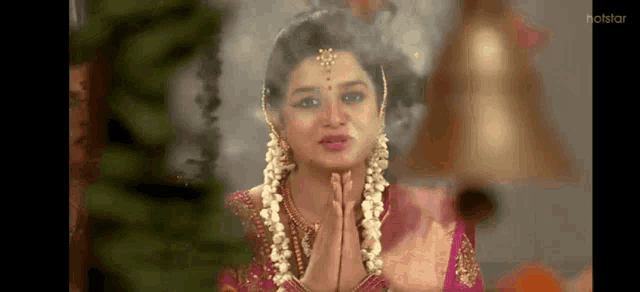 a woman in a pink dress is praying with her hands folded in front of a bell .