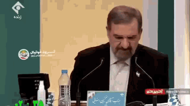 a man in a suit and tie is speaking into a microphone while sitting at a table