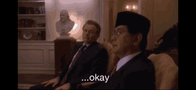 two men are sitting on a couch and one of them says " okay "