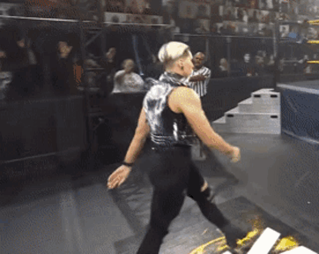 a wrestler in a metallic vest is walking on a mat