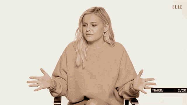 a woman in a tan sweater is sitting in a chair with her hands outstretched in front of a screen that says elle