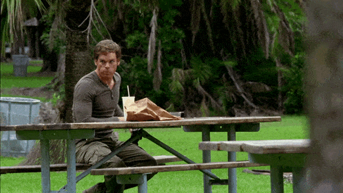 a man sits at a picnic table with a bag and a drink