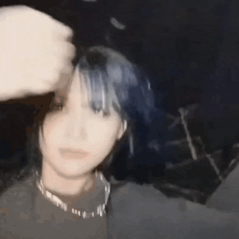a woman with blue hair is taking a selfie with her hand on her forehead .
