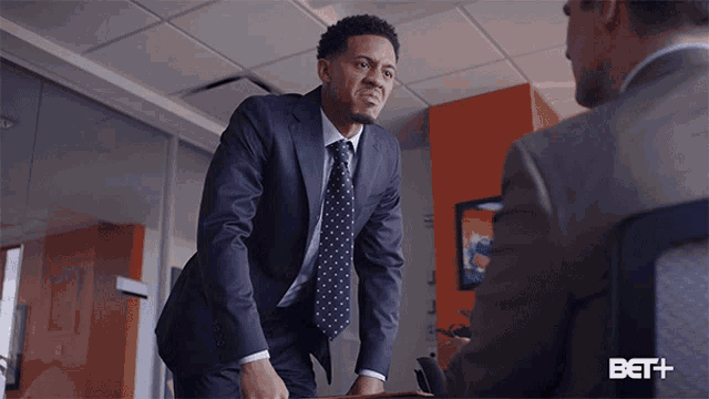 a man in a suit and tie is talking to another man in an office with the bet logo on the bottom right