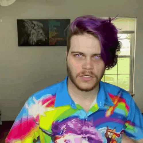 a man with purple hair and a beard wears a colorful shirt