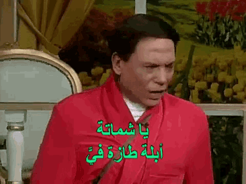 a man in a red robe is sitting in a chair with a picture of flowers in the background .