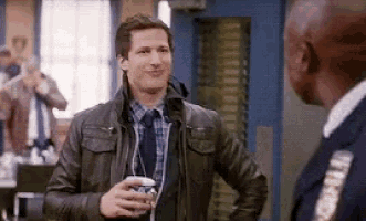a man in a leather jacket and tie is talking to a police officer in a room .