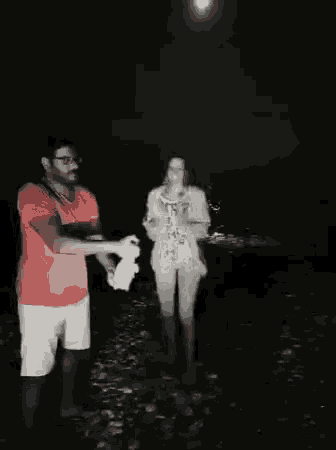 a man and a woman are standing next to each other on the beach at night .